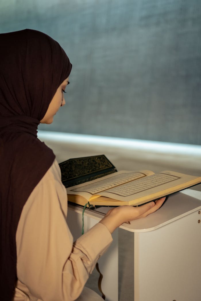 Mastering the First Impression: Your intriguing post title goes here A woman in a hijab peacefully reads the Quran indoors, capturing a serene spiritual moment.